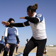 Surfcamp para principiantes con monitor explicando la técnica a una alumna en la playa.
