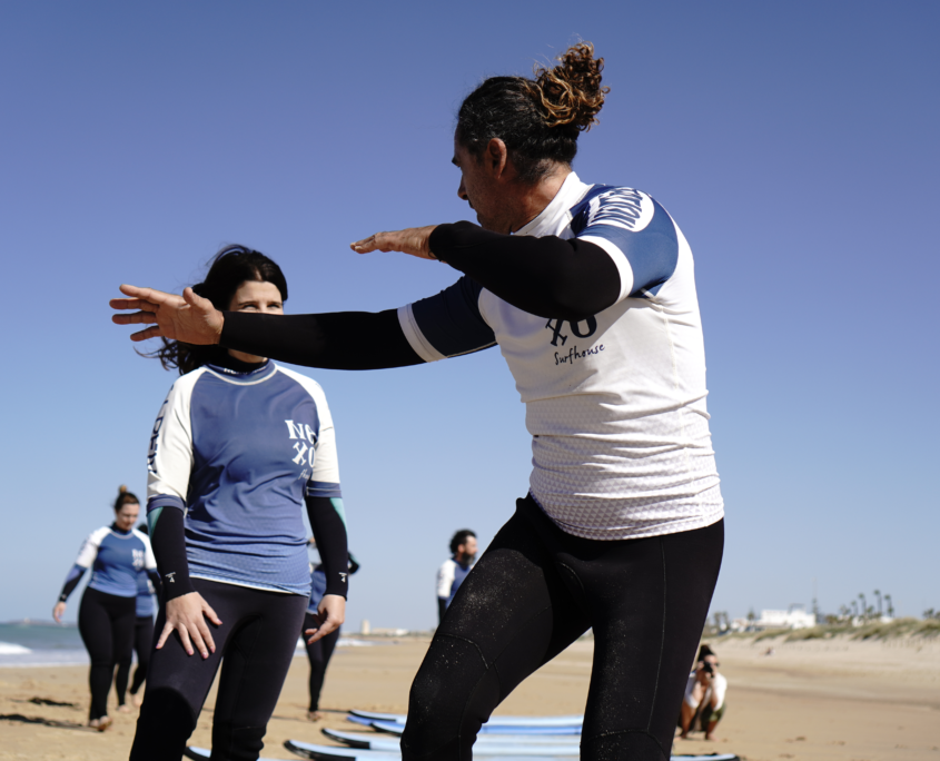 Surfcamp para principiantes con monitor explicando la técnica a una alumna en la playa.