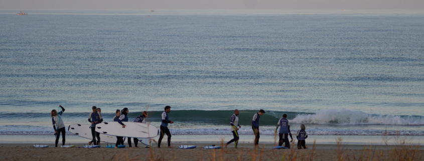 Surfcamp en El Palmar con grupo de surfistas entrenando en la orilla mientras otros esperan olas en el mar.