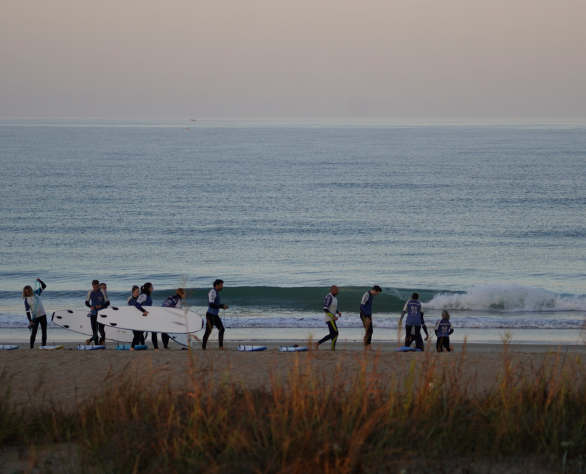 Surfcamp en El Palmar con grupo de surfistas entrenando en la orilla mientras otros esperan olas en el mar.