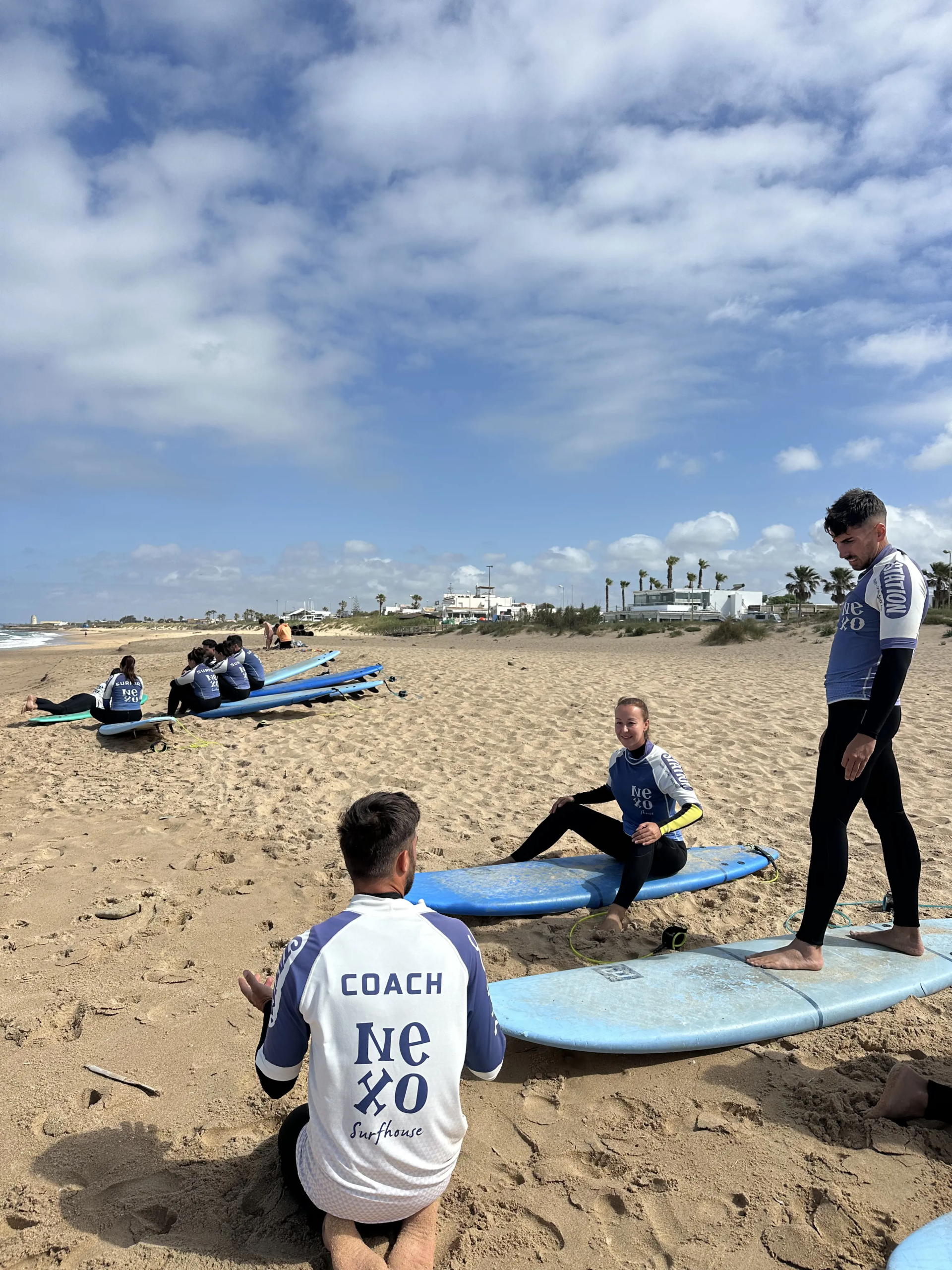 Coach de NEXO explicando técnica de surf a varios alumnos en El Palmar